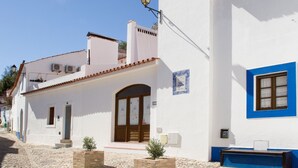 Una calle adoquinada con edificios blancos y marcos de ventanas azules, además de un pequeño banco.