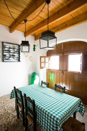 A dining area with a checkered tablecloth, wooden chairs, a hanging lantern, and a window with wooden shutters. - Casas de Romaria de Brotas (Mora)