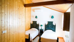 Una habitación con dos camas, paredes de madera, un ventilador de techo y una pequeña mesa con una lámpara.
