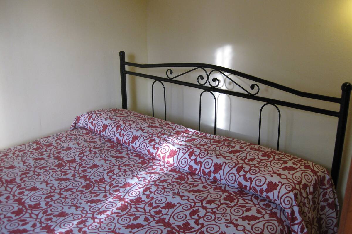 Ein Einzelbett mit Metallgestell und einem gemusterten Bettbezug.