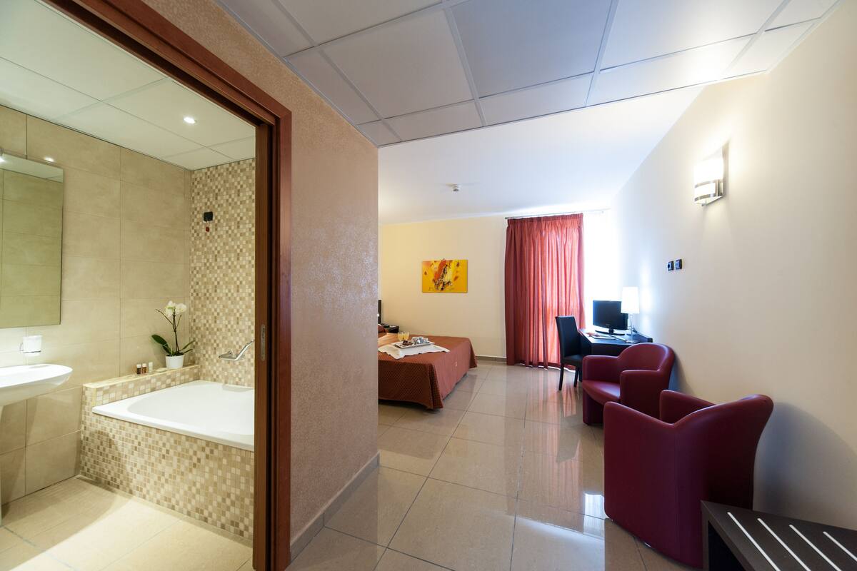 A hotel room with a bathroom, a bed, a desk, and a chair.