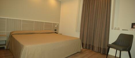 A bedroom with a bed, a chair, a nightstand, and a window with curtains.