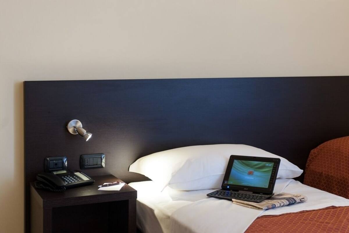 A hotel room with a bed, a desk with a phone and a lamp, and a laptop on the bed.