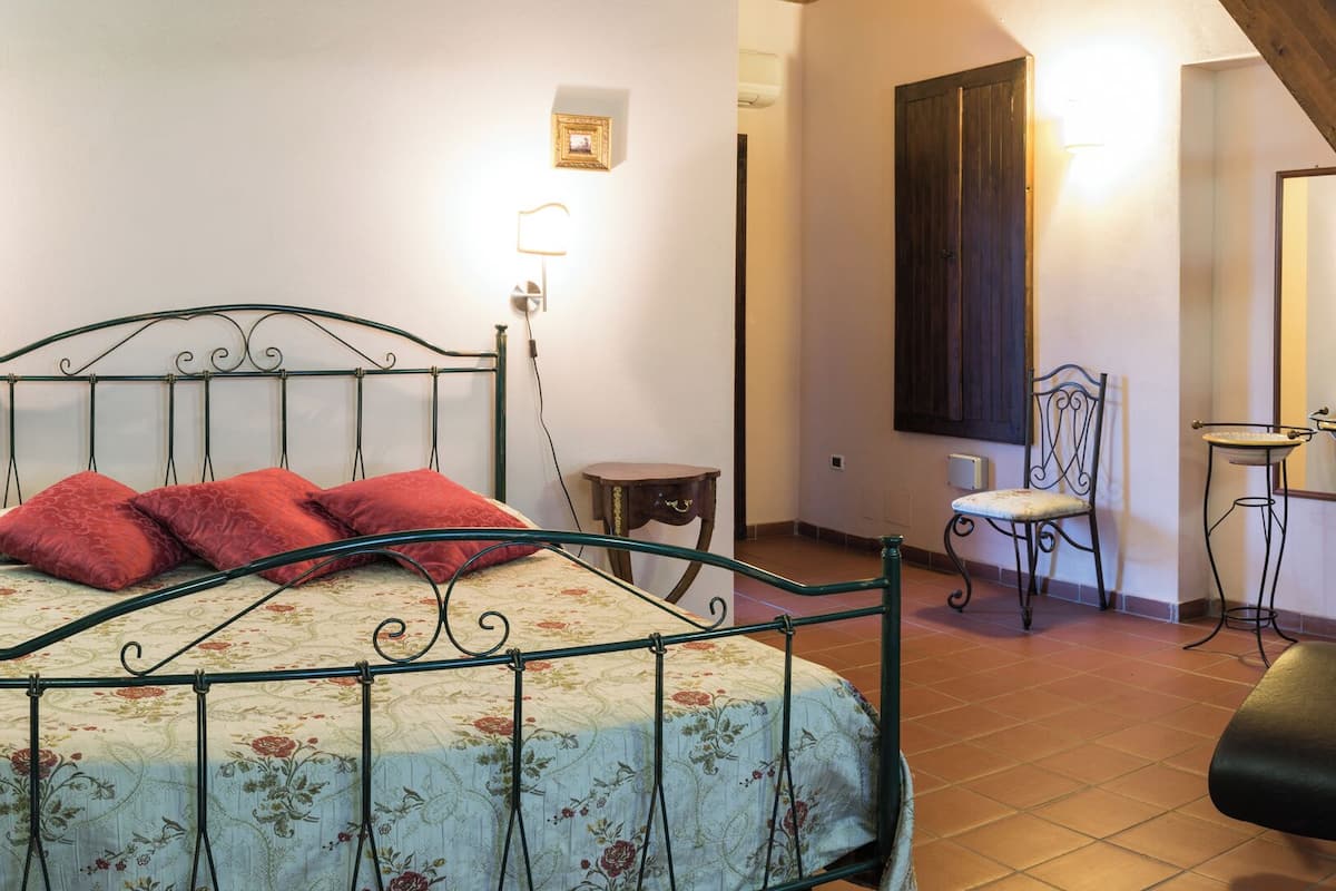 Un dormitorio con cama, mesitas de noche, una silla, un escritorio, una lámpara, un espejo y una escalera.
