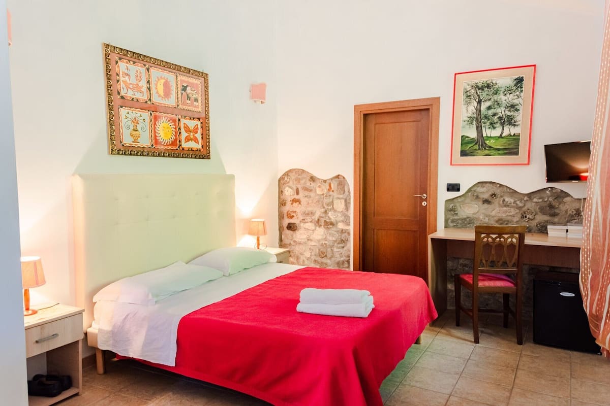 Un dormitorio con cama, escritorio, silla, puerta y un cuadro en la pared.