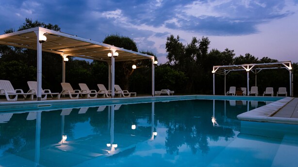 Une piscine avec des chaises longues et un espace abrité éclairé.