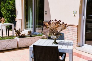 An outdoor seating area with a table and chairs, a decorative vase with dried flowers, and a brick wall with numbered signs.