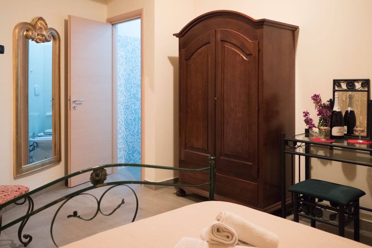 Un dormitorio con una cama, un armario de madera, una mesa de vidrio y copas de vino, y un espejo.