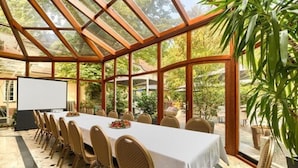 Een vergaderzaal met een lange tafel, stoelen, een projectiescherm en een glazen dak.