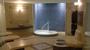 Een badkamer met een mozaïek tegelontwerp, een centrale fontein en meerdere zitgedeeltes.