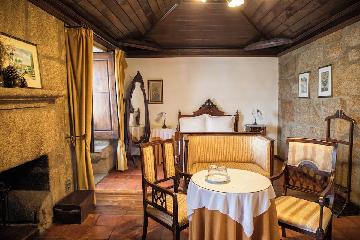 Una habitación acogedora con pared de piedra, techo de madera y chimenea. Hay una mesa con sillas y un banco.