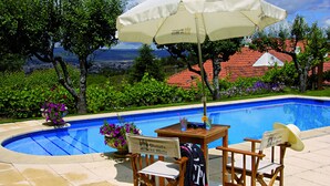 A poolside area with a view of a cityscape, a table with chairs, and an umbrella. - Quinta da Mata (Chaves)