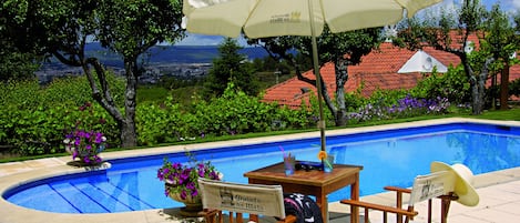 A poolside area with a view of a cityscape, a table with chairs, and an umbrella.