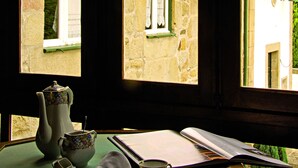 A room with a view through a window, a table with a book, a teapot, and a cup. - Quinta da Mata (Chaves)