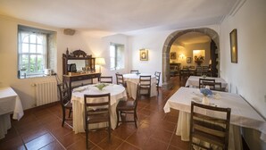 A dining area with multiple tables and chairs, a fireplace, and a view through an archway to another room. - Casa dos Assentos de Quintiães (Barcelos)