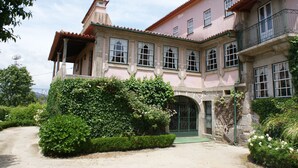A two-story building with a pink facade, a covered porch, and a green door. - Casa dos Assentos de Quintiães (Barcelos)