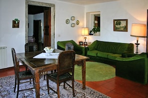 Zona pranzo con tavolo e sedie in legno, un divano verde e una lampada.