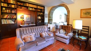 A cozy living room with a grey sofa, armchairs, and a bookshelf filled with books. - Casa dos Assentos de Quintiães (Barcelos)