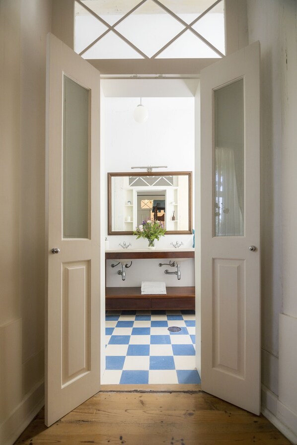 Puerta abierta que da a un baño con piso a cuadros, un espejo y un lavamanos.