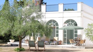 Un edificio con facciata bianca, ampie finestre ad arco e una zona esterna coperta con sedie e tavoli.