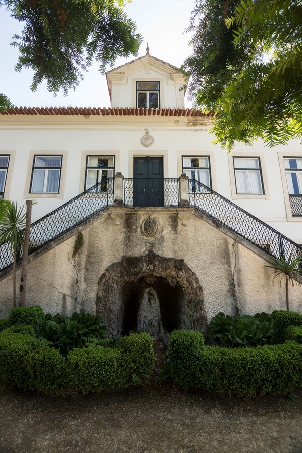 Un edificio con fachada blanca, puerta negra y una escalera de piedra que conduce a un balcón.