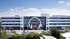 A modern hotel with a prominent arch entrance, multiple floors, and a parking lot with several cars.