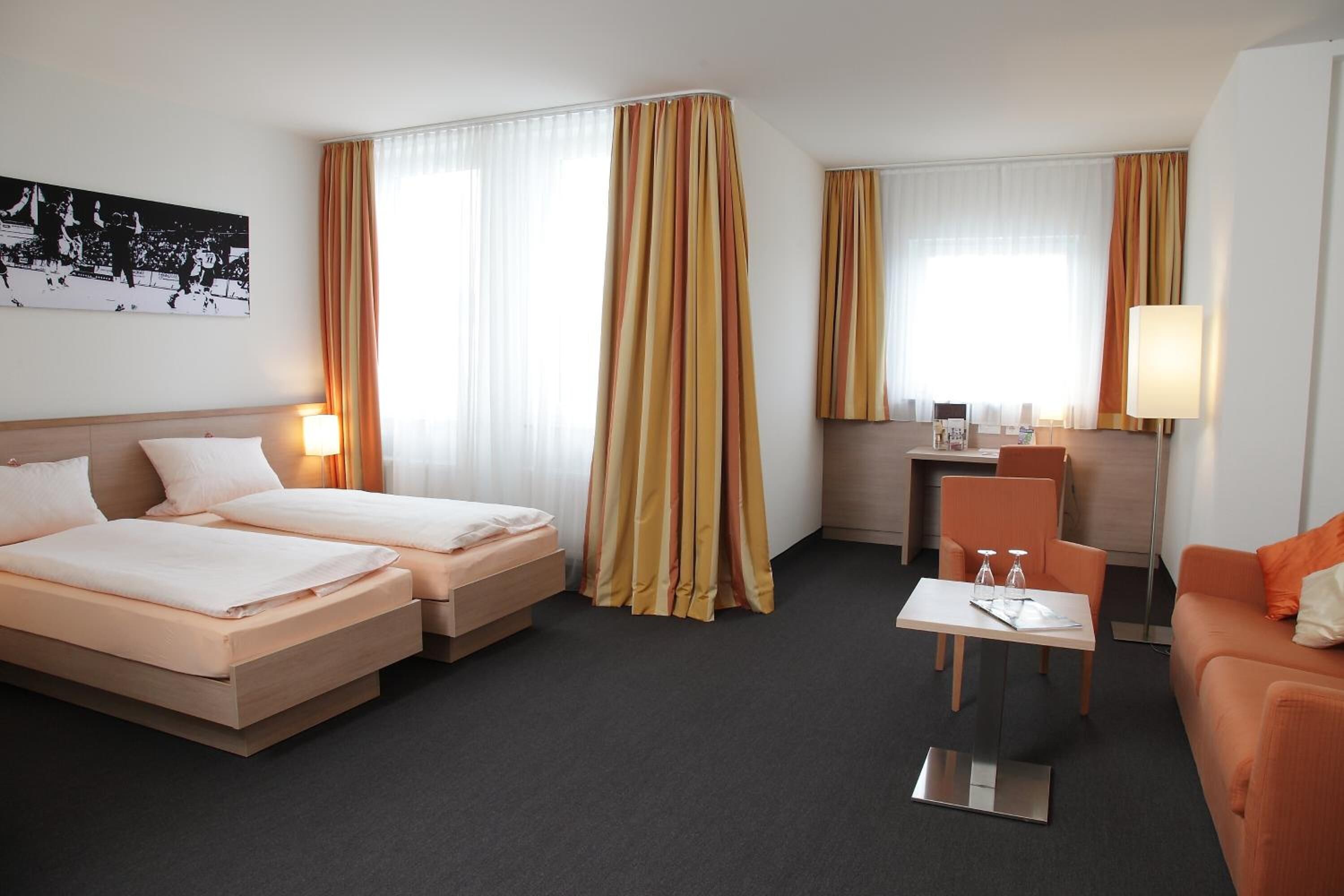 A hotel room with two beds, a desk, a chair, and a sofa.