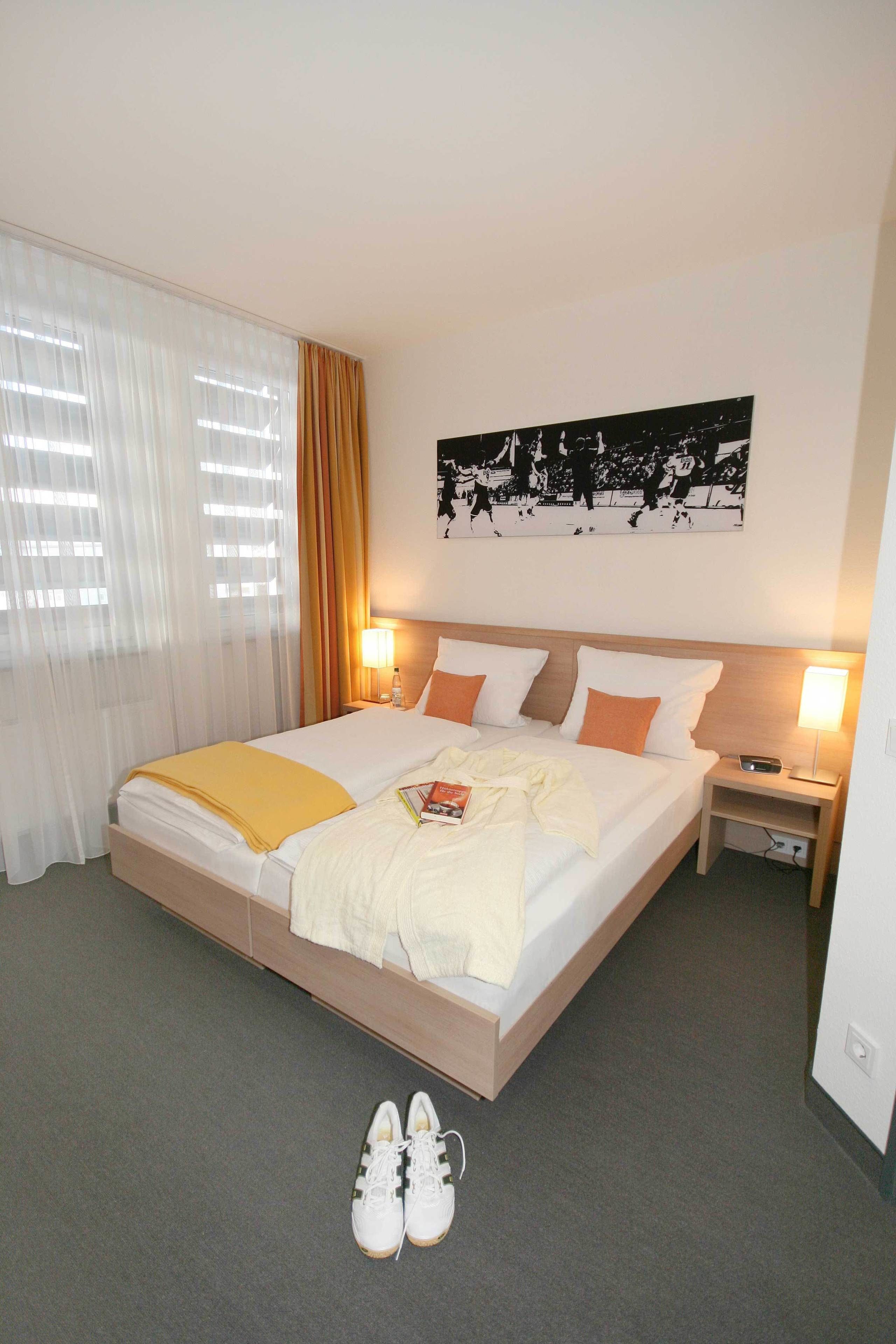 A hotel room with a large bed, a bedside table with a lamp, a wall-mounted artwork, and a pair of shoes on the floor.