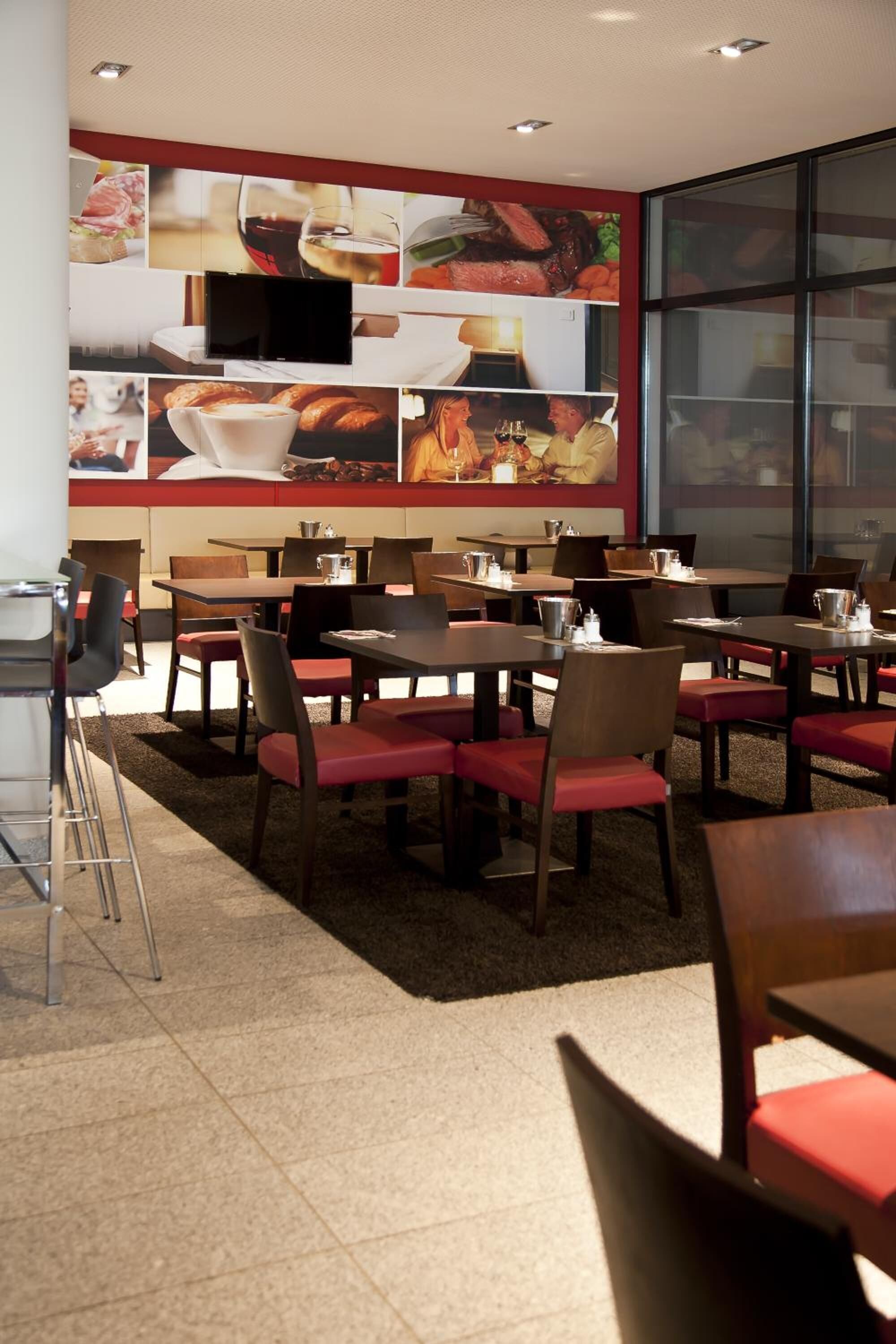Un restaurant doté de nombreuses tables et chaises, d’un grand mur orné d’images de plats et de boissons, et d’un écran de télévision.