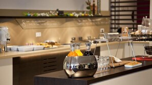 A buffet setup with a variety of food items and beverages, including a glass container with orange juice and a bottle of water.