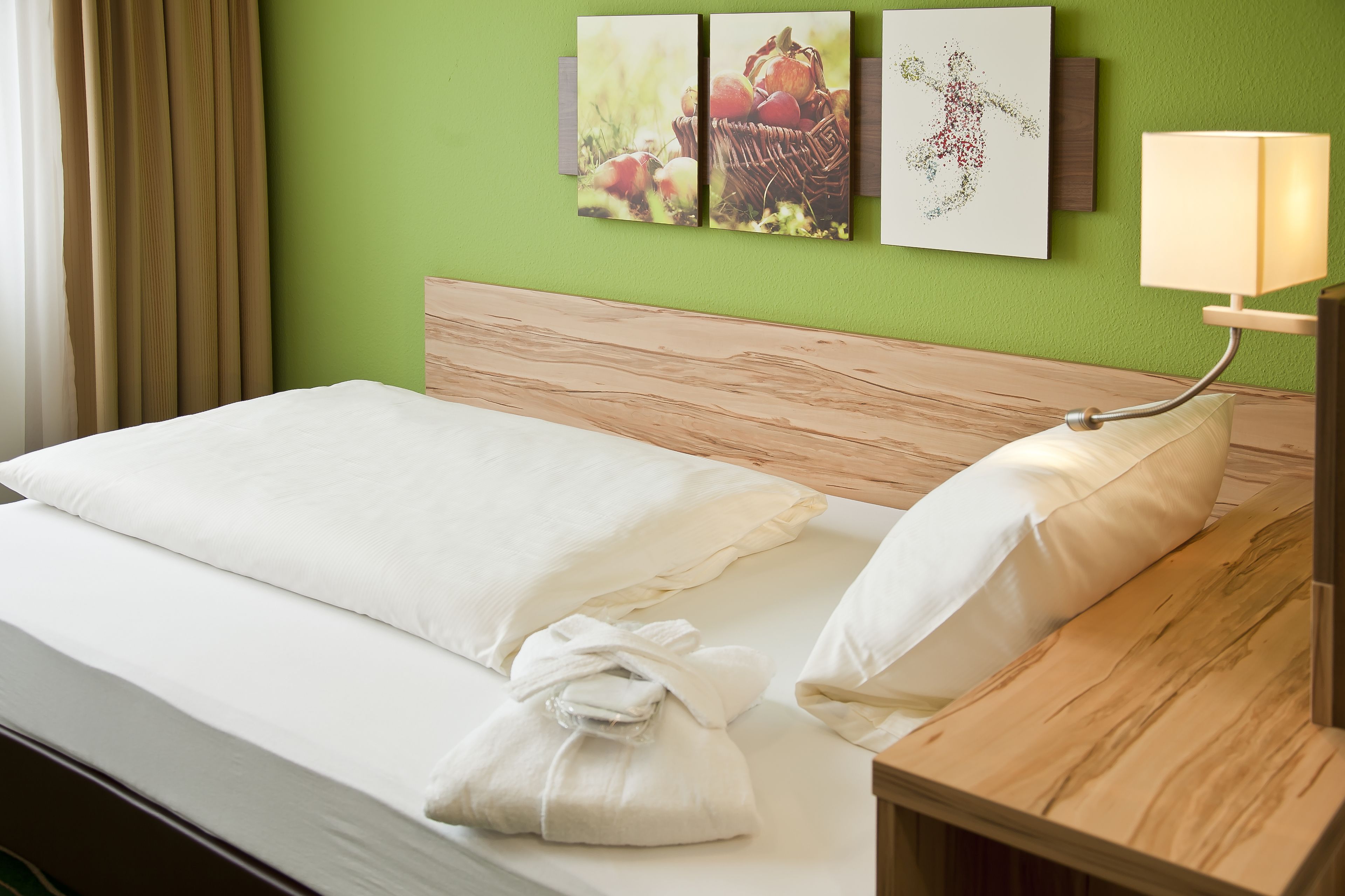 A neatly made bed with white linens, a wooden headboard, and a bedside table with a lamp.