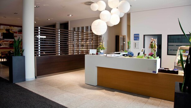 A modern reception area with a wooden reception desk, white walls, and a large plant.