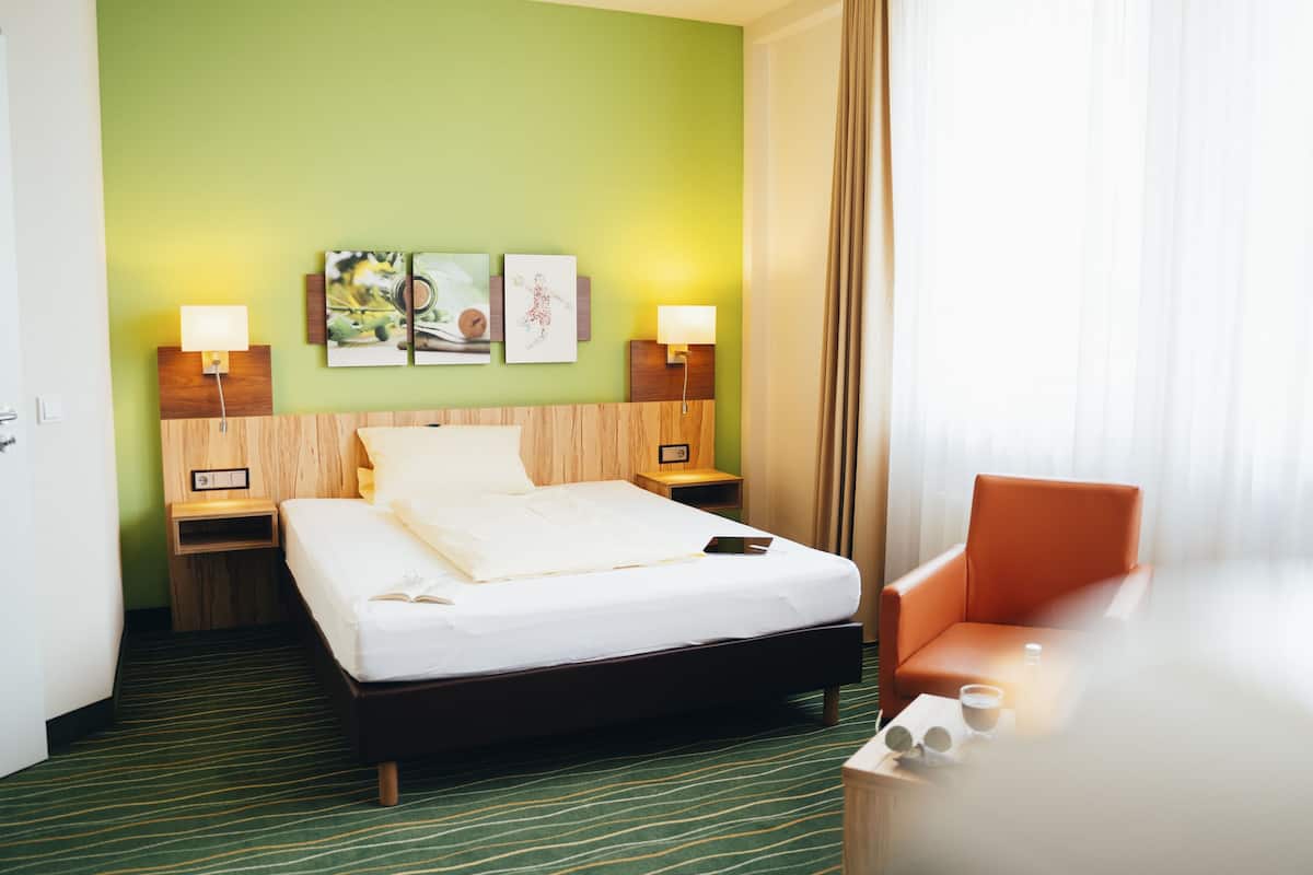 A hotel room with a bed, two bedside tables with lamps, a chair, and artwork on the wall.