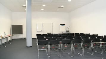Un salón de conferencias con filas de sillas, un proyector, una pizarra y una pantalla para presentaciones.