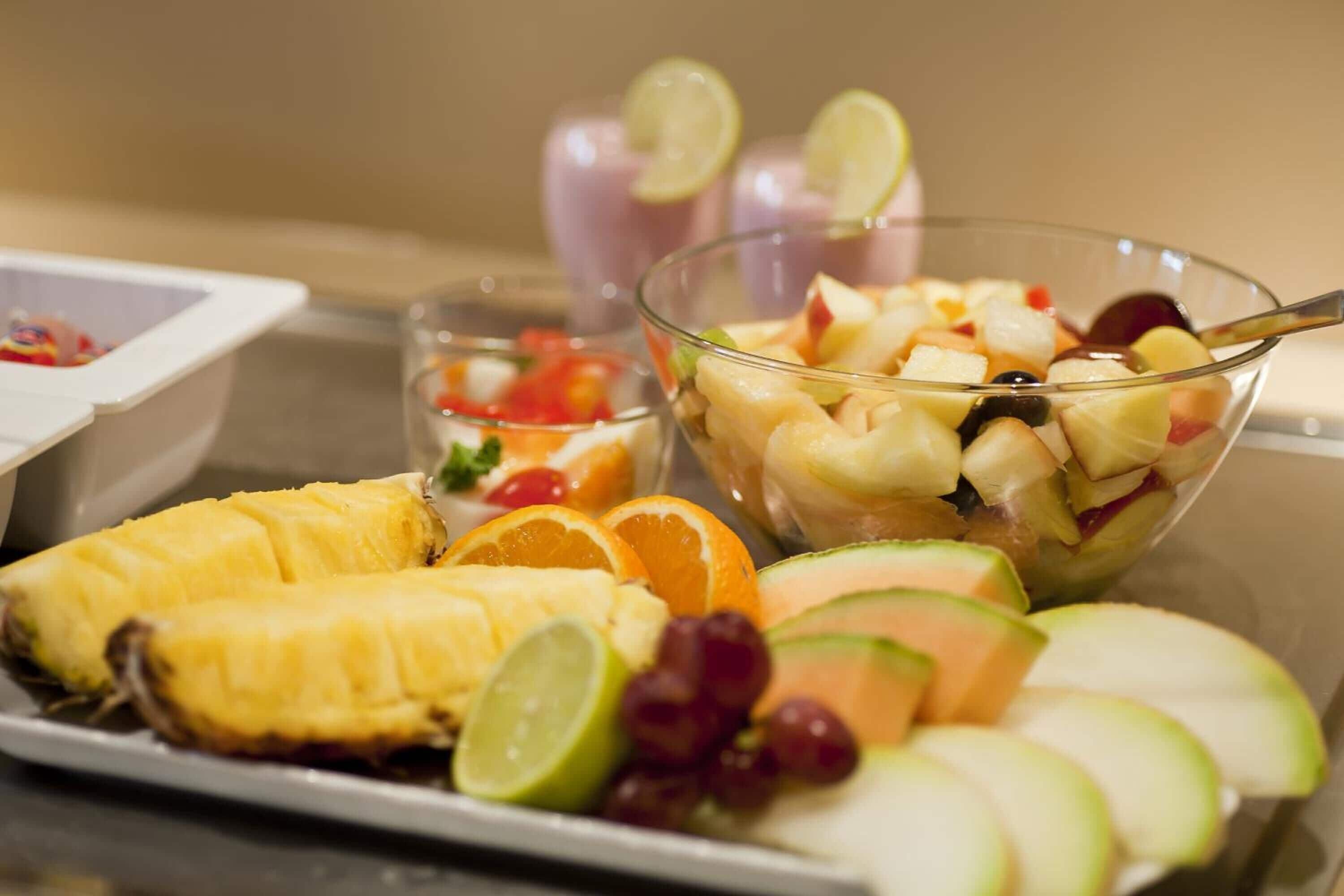 Una bandeja de frutas con piña, naranjas, uvas y melón en rodajas.