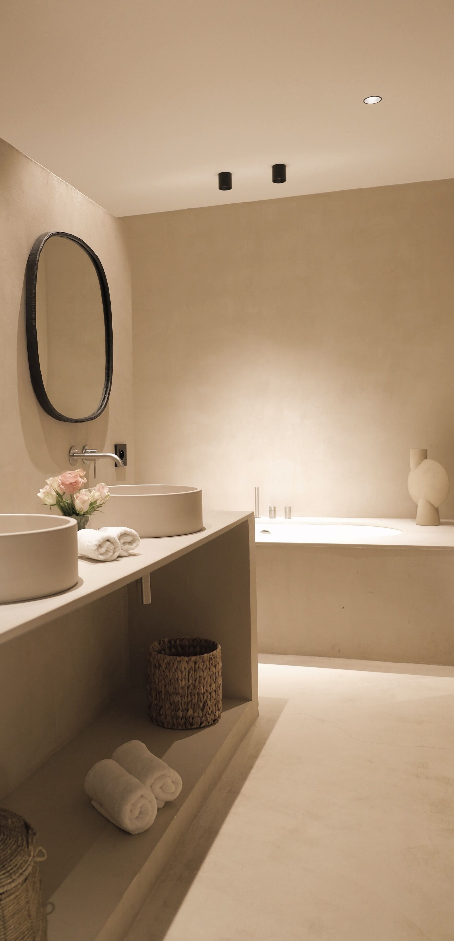 Une salle de bain moderne avec un grand miroir, deux lavabos, une baignoire et un petit panier en osier.