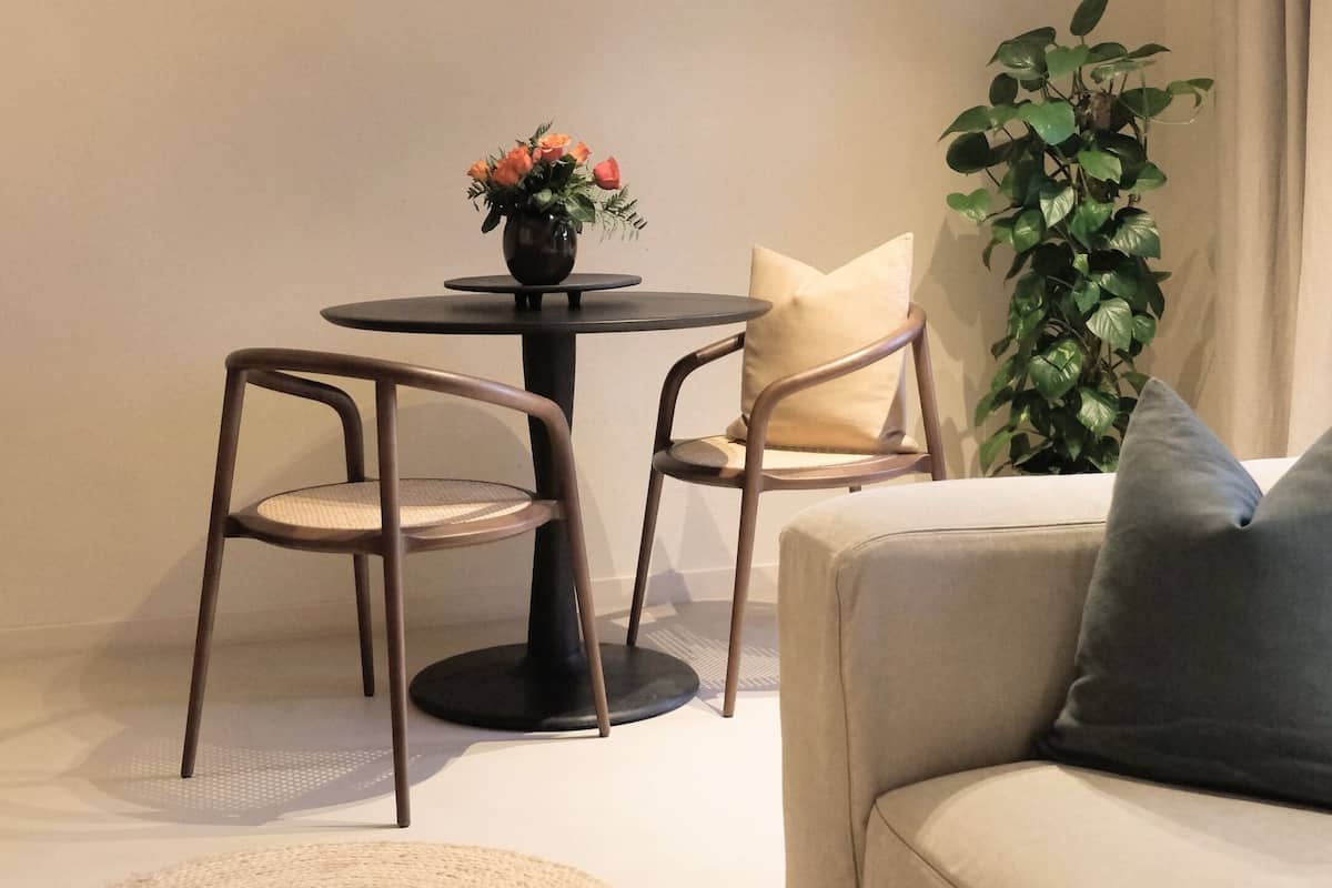 A modern living room with a round dining table, two chairs, a sofa, a potted plant, and a woven rug.