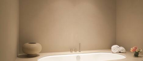 A modern bathroom with a large bathtub, a round vase, and neatly rolled towels.