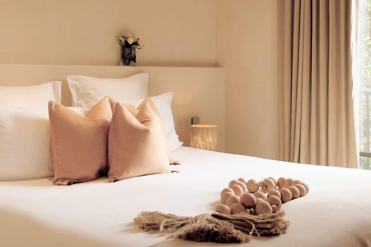 A neatly made bed with white and pink pillows, a bedside lamp, and a decorative arrangement of eggs on the bed.