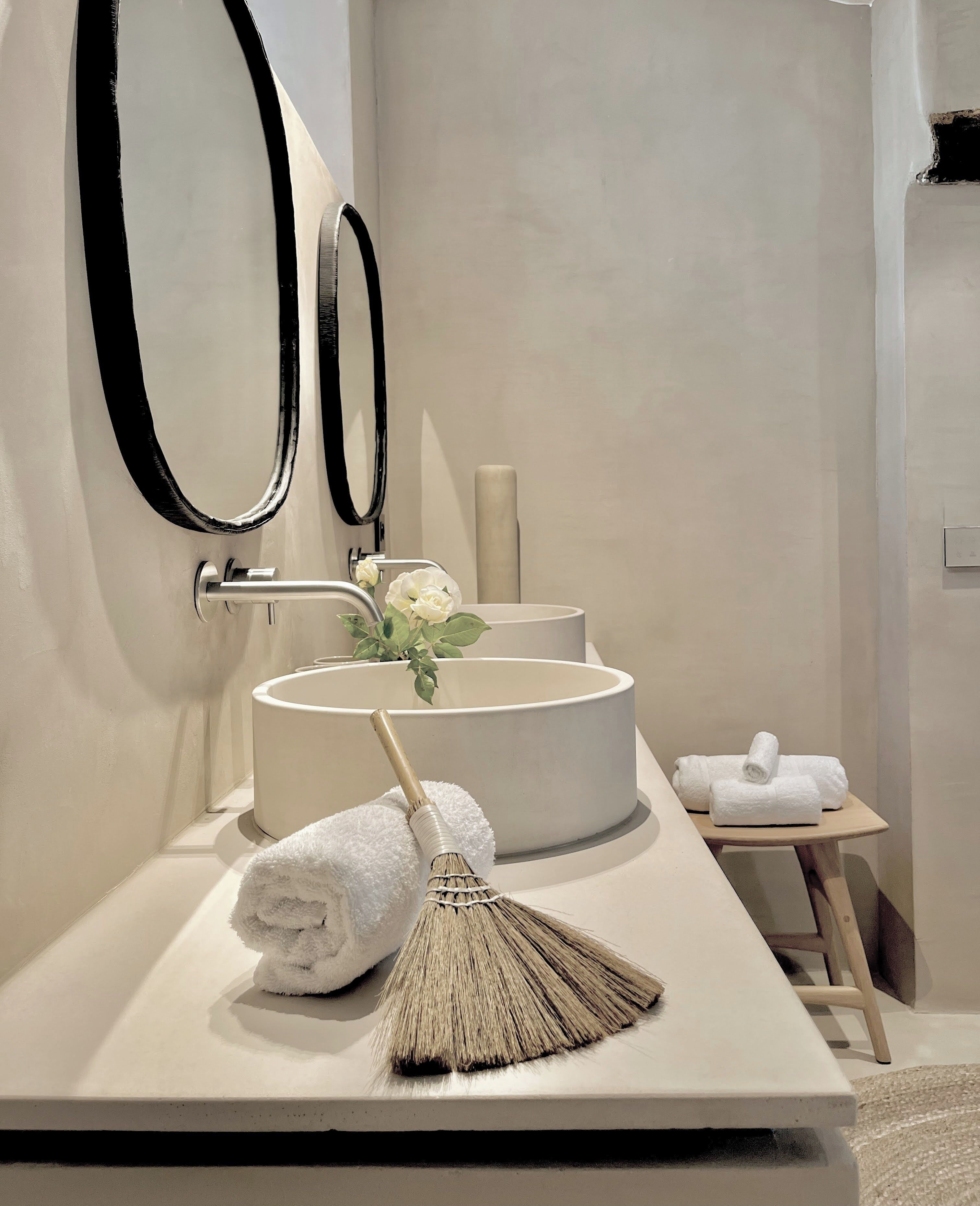 Un bagno moderno con un lavabo rotondo grande, due specchi fissati al muro, un piccolo tavolo con asciugamani e una scopa.