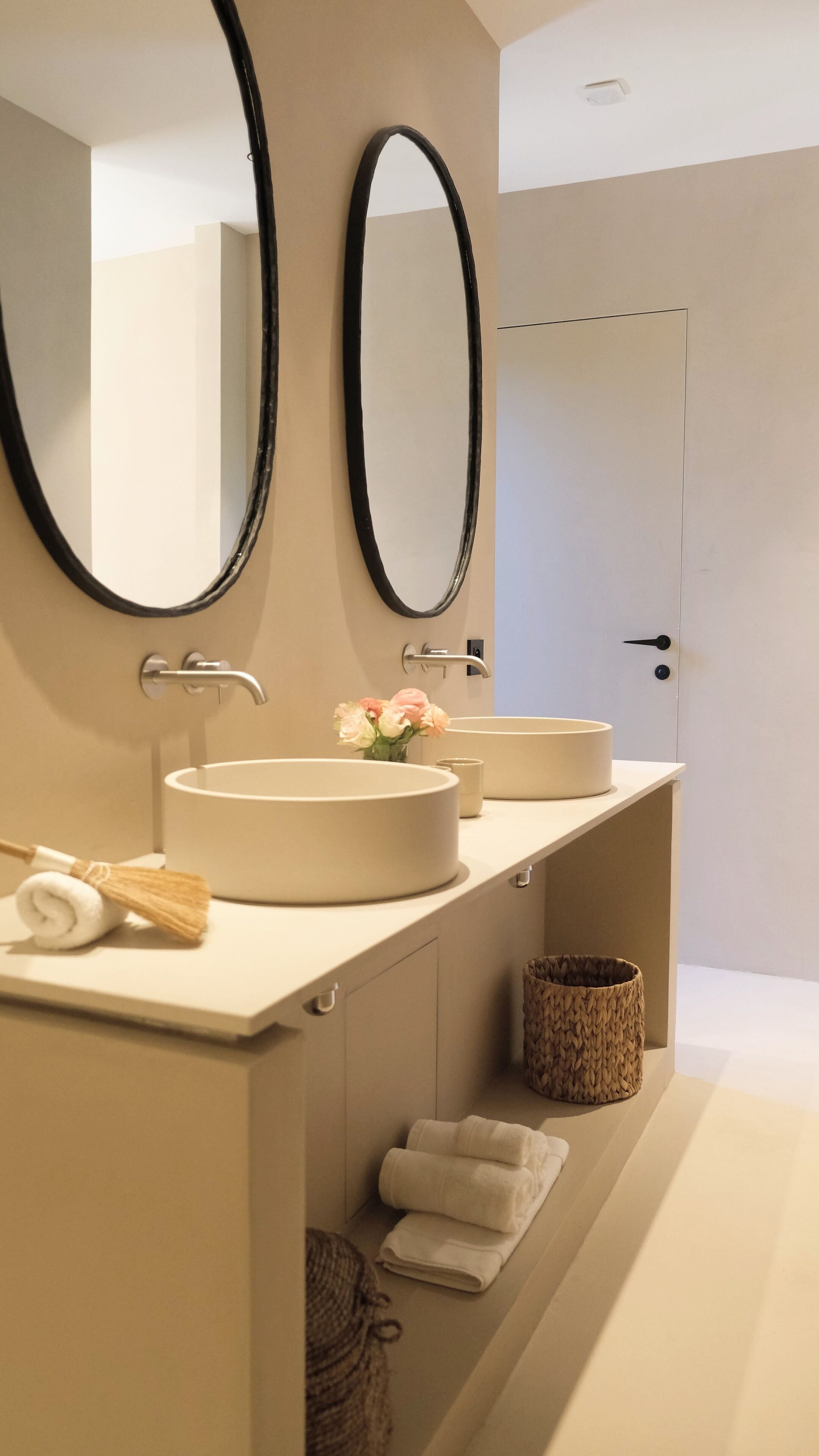 A modern bathroom with two oval mirrors, a round sink, and a towel rack.