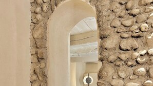 A stone archway leading to a bedroom with a bed and a floor lamp. - Toile Blanche (Saint-Paul-de-Vence)