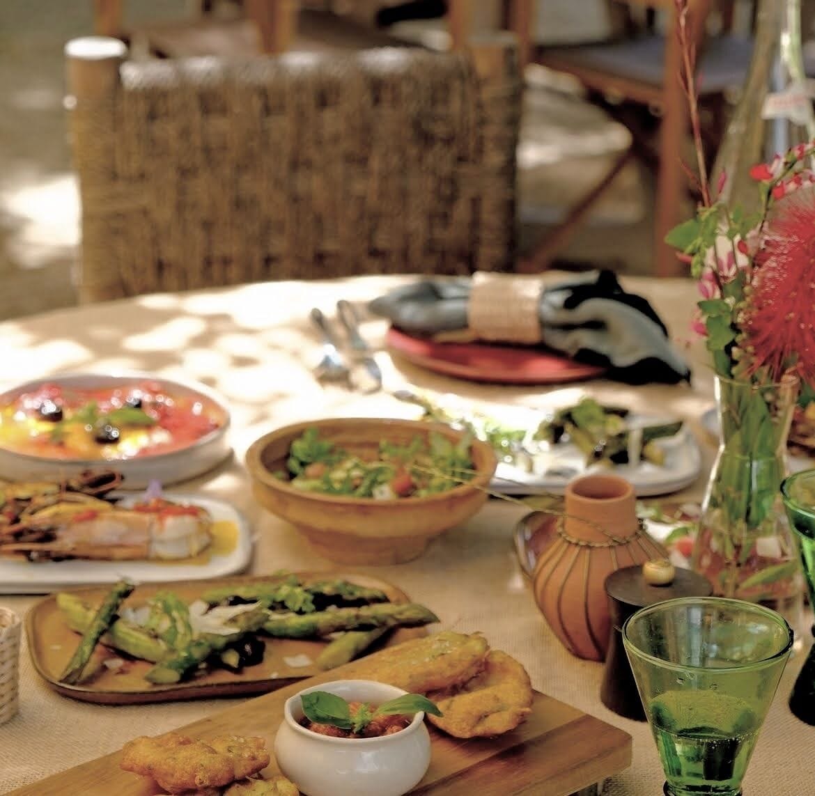 Een eettafel met verschillende gerechten, een vaas met bloemen en een groen glas.