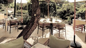 An outdoor dining area with tables and chairs under a large tree, surrounded by umbrellas and lanterns. - Toile Blanche (Saint-Paul-de-Vence)