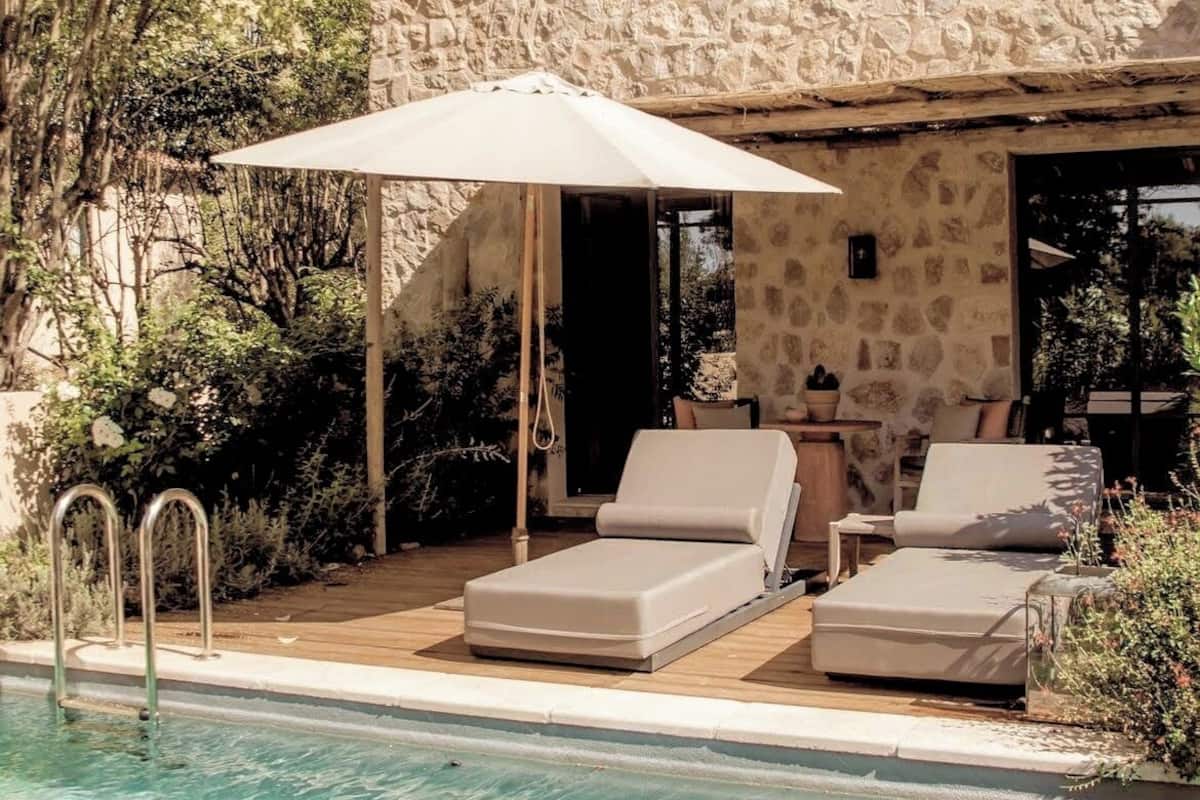 A pool area with lounge chairs and a canopy, surrounded by stone walls and greenery.