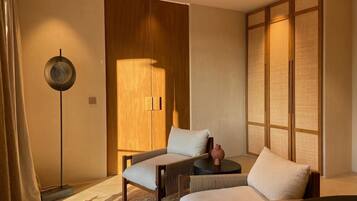 A modern bedroom with a bed, two chairs, a small table, and a traditional Japanese room divider.