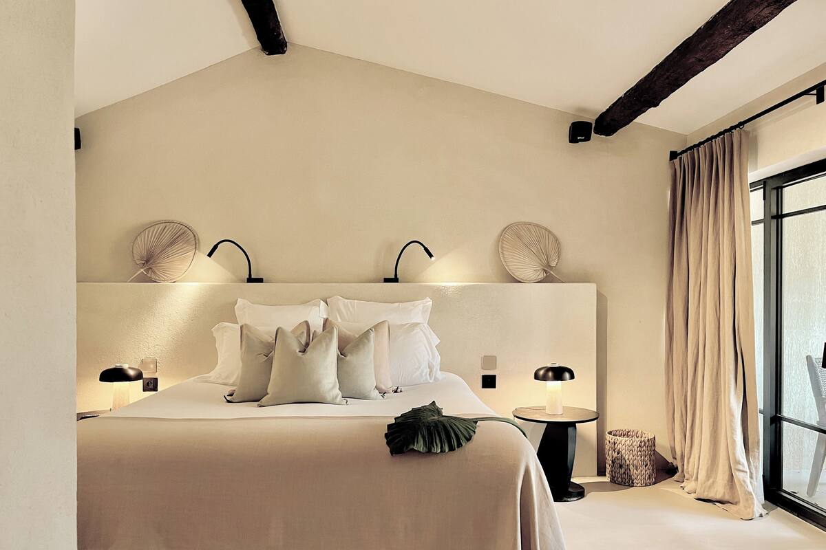 A modern hotel room with a large bed, two bedside tables, and a large window with curtains.