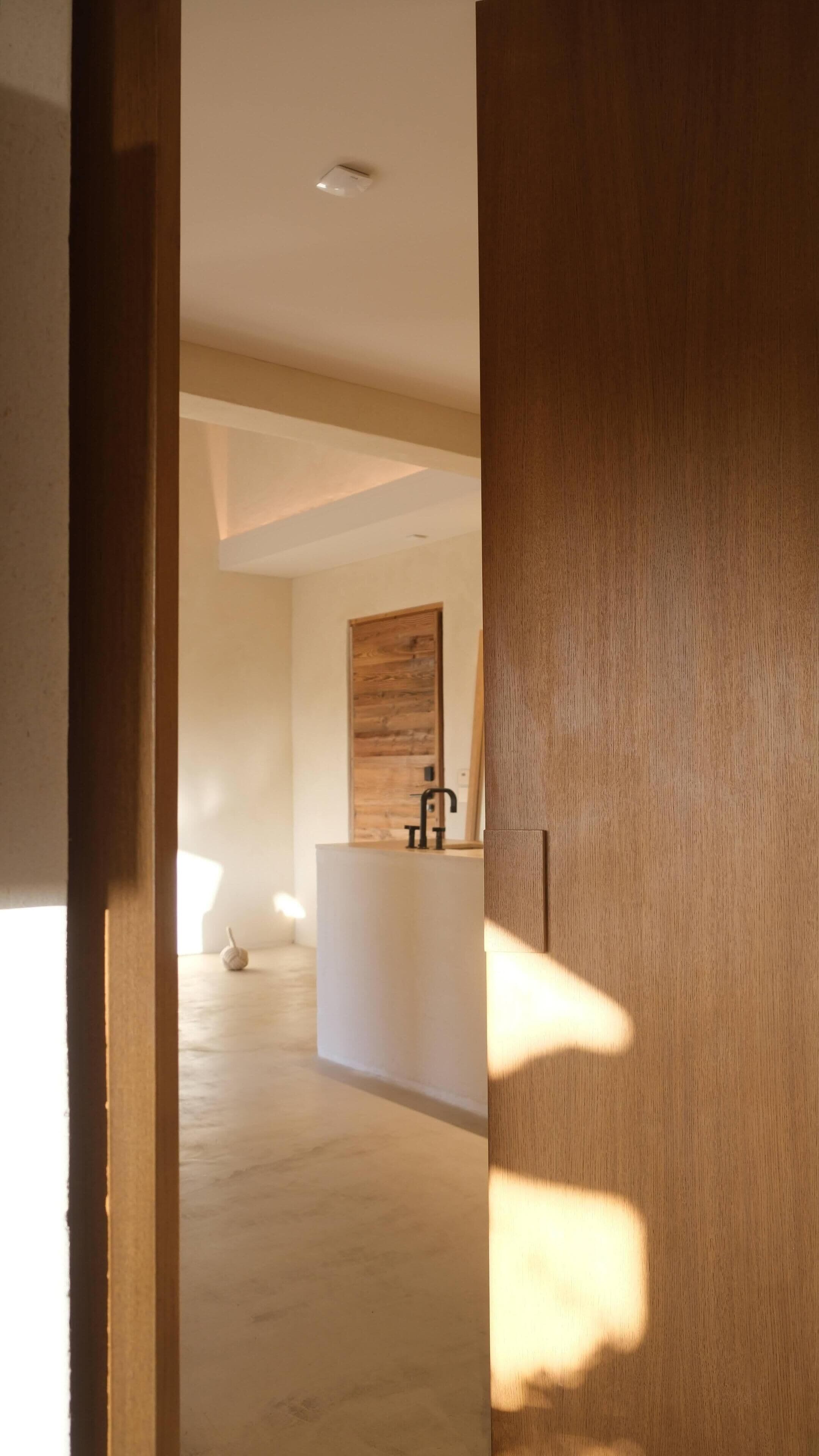 A modern bathroom with a wooden vanity, a black faucet, and a wooden door in the background.