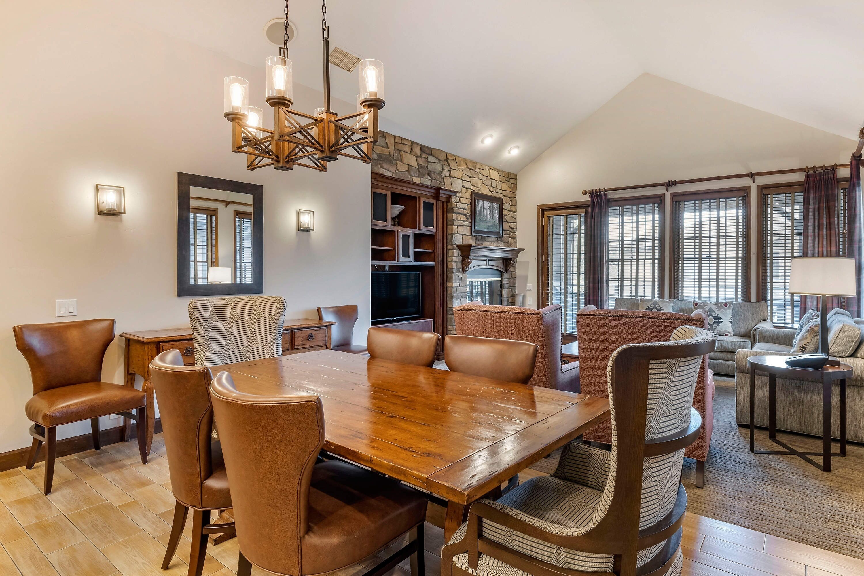 A spacious living area with a large wooden dining table surrounded by leather chairs, a stone fireplace, and a cozy seating area with sofas and a television.