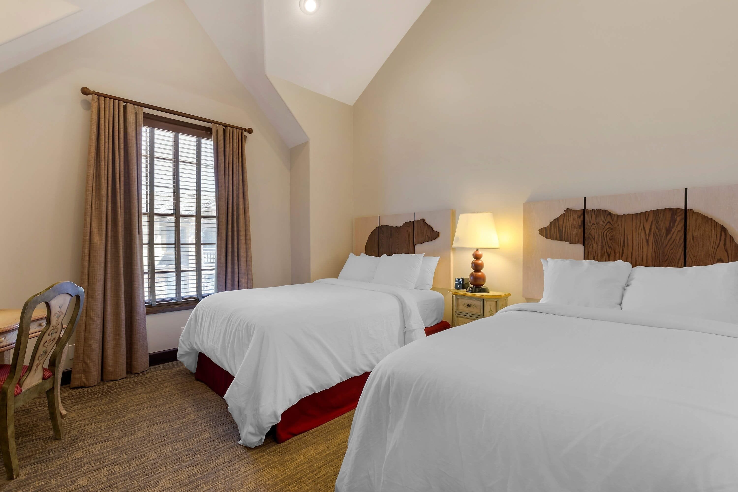 A hotel room with two beds, a desk, and a chair.